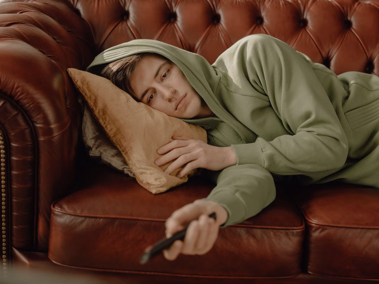 Ung man i grön hoodie ligger i soffan