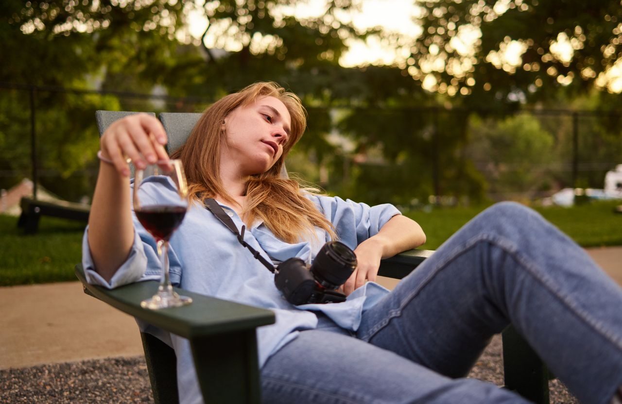 Kvinna sitter i en stor i trädgården med ett glas vin